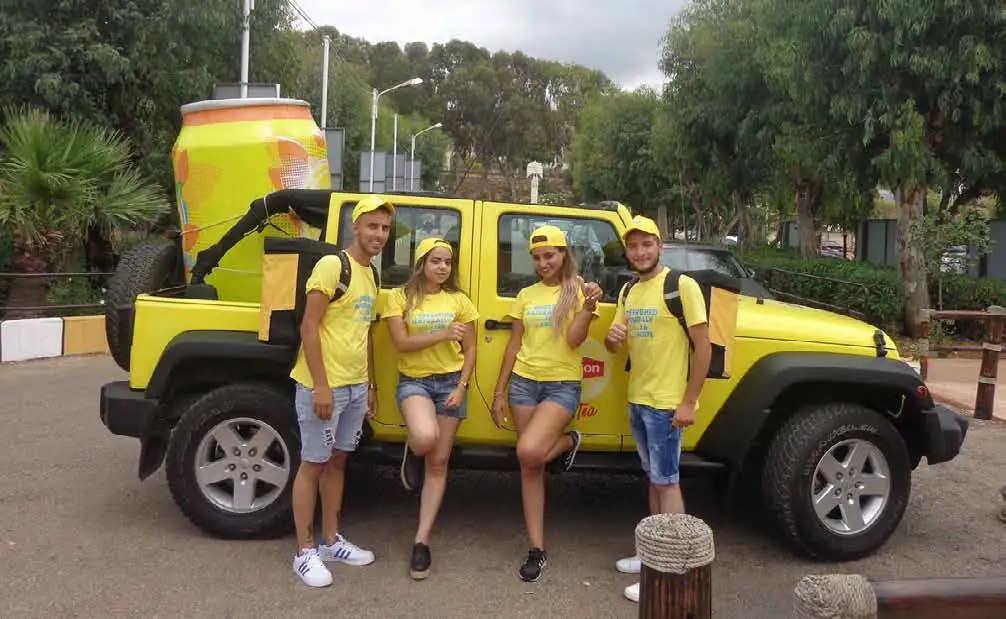 Promoters in yellow Lipton T-shirts beside a branded jeep with a giant can on its roof