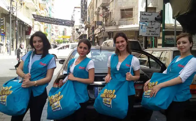 Four promoters in blue vests handing out branded bags on a city street