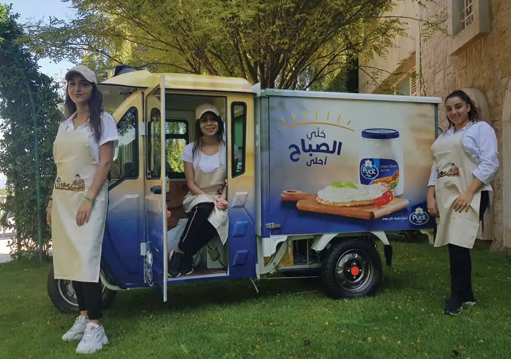 Puck promoters in aprons beside a Puck-branded tuk-tuk
